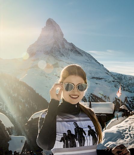 Woman smiling with sunglasses in a sunny ski area in front of the Matterhorn.