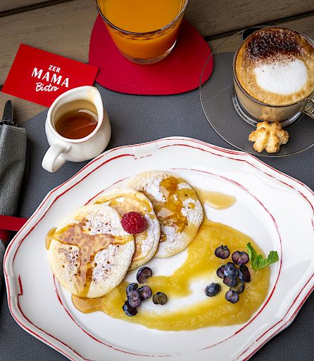 Pancakes with berries and syrup, served with coffee and orange juice on a table.