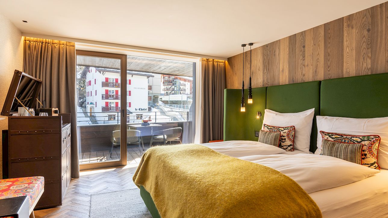 Modernes Hotelzimmer mit Doppelbett, grünen Akzenten, Balkon und Blick auf schneebedeckte Gebäude.