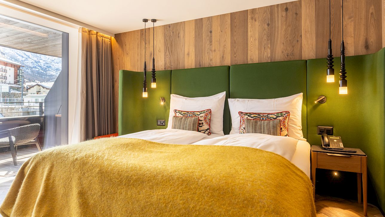 Modernes Hotelzimmer mit großem Doppelbett, grünem Kopfteil und Balkon mit Bergblick.