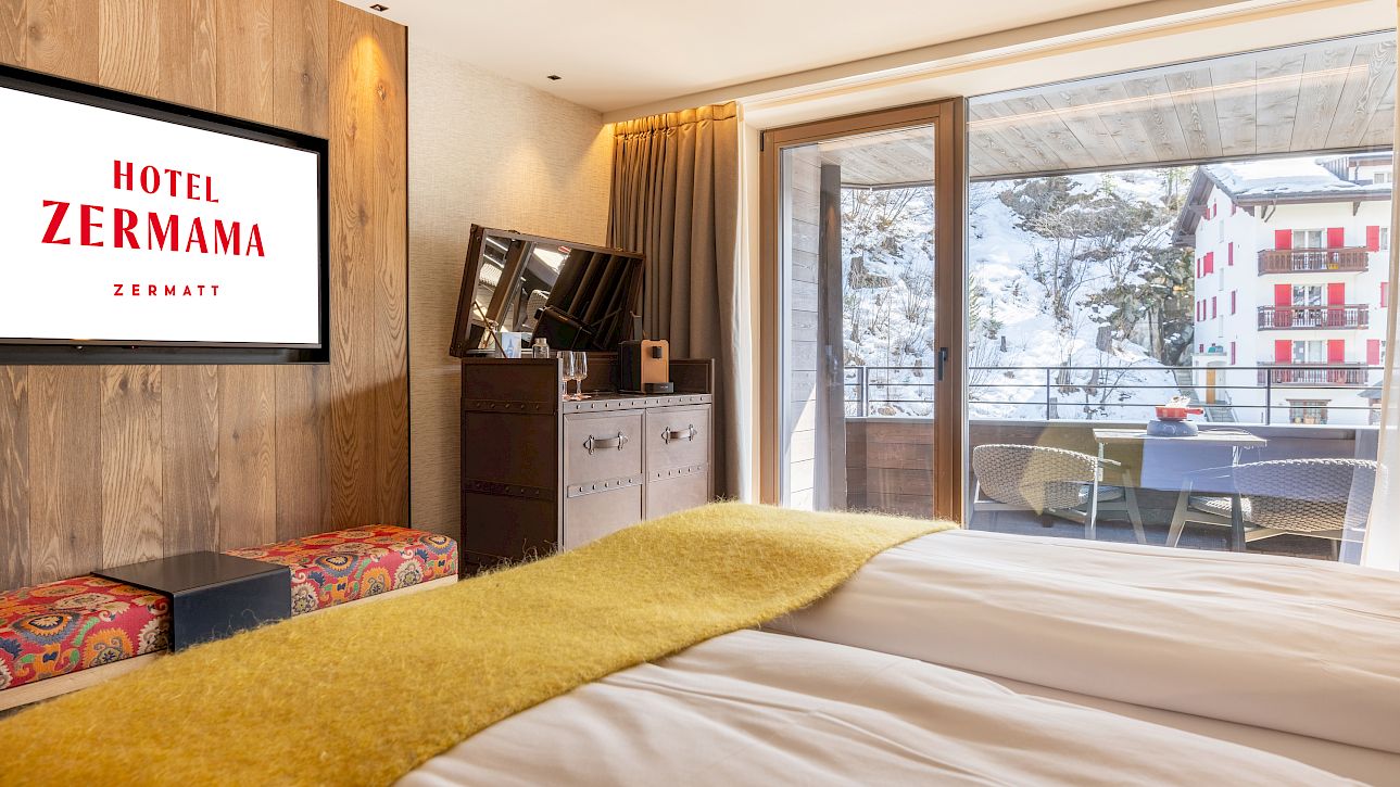 Gemütliches Hotelzimmer mit Bergblick, großem Bett, Fernseher und Balkon. Schöne helle Holzmöbel.