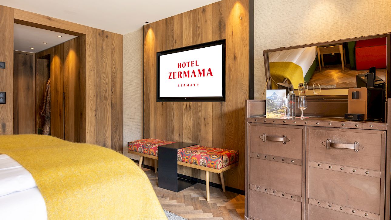 Modernes Hotelzimmer mit Holzwänden, TV, Kommode und dekorativem Teppich. Gemütliche Atmosphäre.