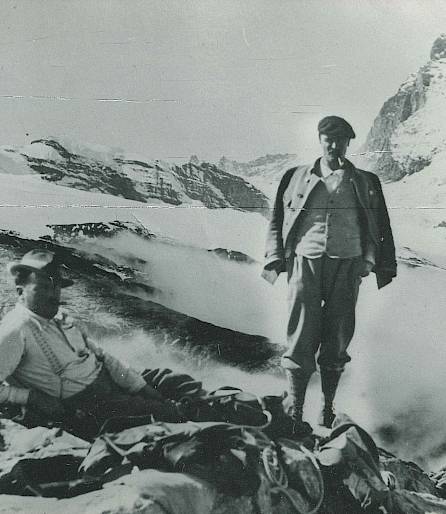 Deux alpinistes posent devant le majestueux Cervin, entourés de sommets enneigés et de nuages.