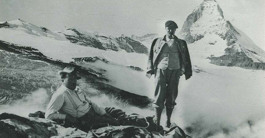 Deux alpinistes posent devant le majestueux Cervin, entourés de sommets enneigés et de nuages.
