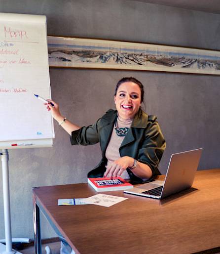 Frau präsentiert lächelnd Geschäftsstrategien auf einem Flipchart, Laptop und Notizen auf dem Tisch.