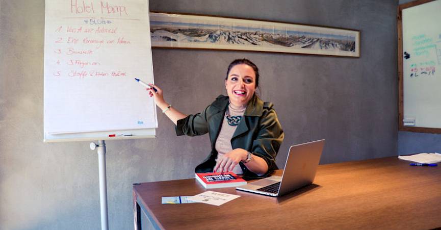 Femme souriante présente des stratégies commerciales sur un tableau, ordinateur portable et notes sur la table.