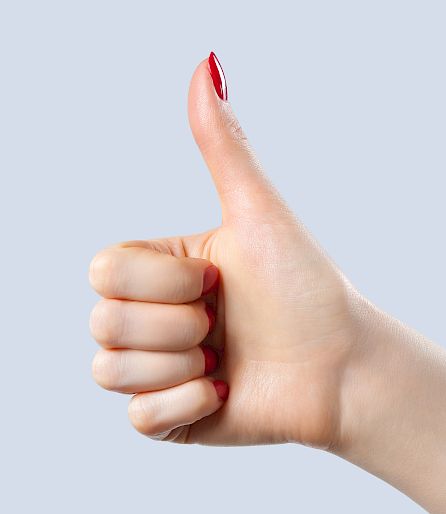 Daumen hoch vor grauem Hintergrund, mit rotem Nagellack; symbolisiert Zustimmung oder positives Feedback.