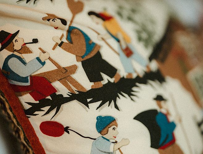 Embroidered pillow with traditional Swiss designs; figures in rural style depicting outdoor activities.