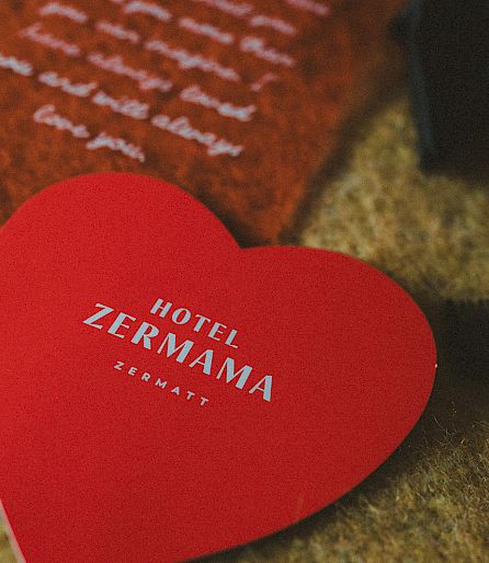 Red heart-shaped sign with "Hotel Zermama" text on a surface, blurred background.