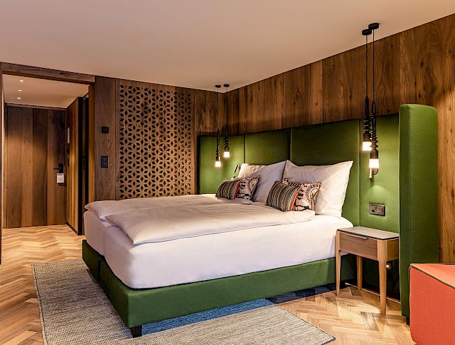 Chambre d'hôtel moderne avec un grand lit vert, des murs en bois et des lampes suspendues élégantes.