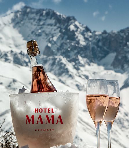 Bouteille de vin pétillant et verres dans la neige, sur fond de montagnes alpines et ciel bleu.