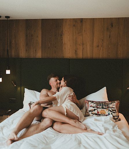Un couple s'enlace tendrement sur un lit confortable dans une chambre moderne et élégante.