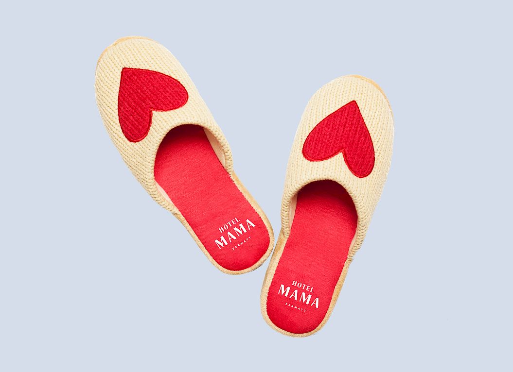 Chaussons beiges avec motifs de cœur rouges sur le dessus, sur fond bleu clair.