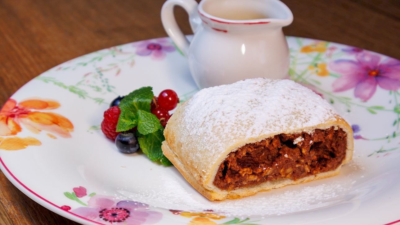 A plate with strudel, fresh berries, and a sauce jug on floral china.