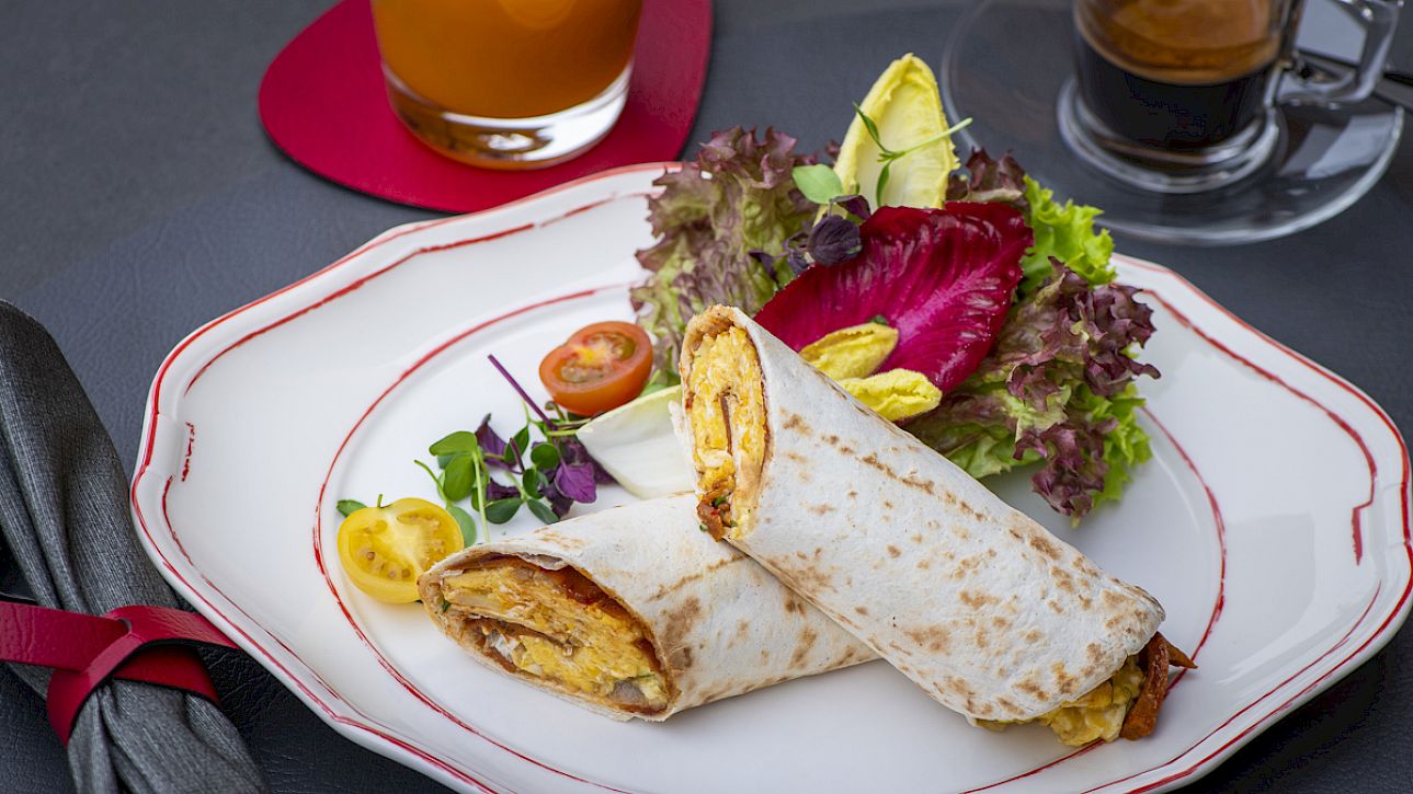 Wrap on a plate with salad, orange juice, and espresso on a table.