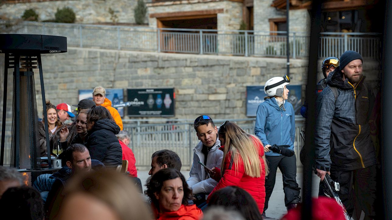 A group of people enjoying a break outdoors in a mountain village, some wearing ski gear.