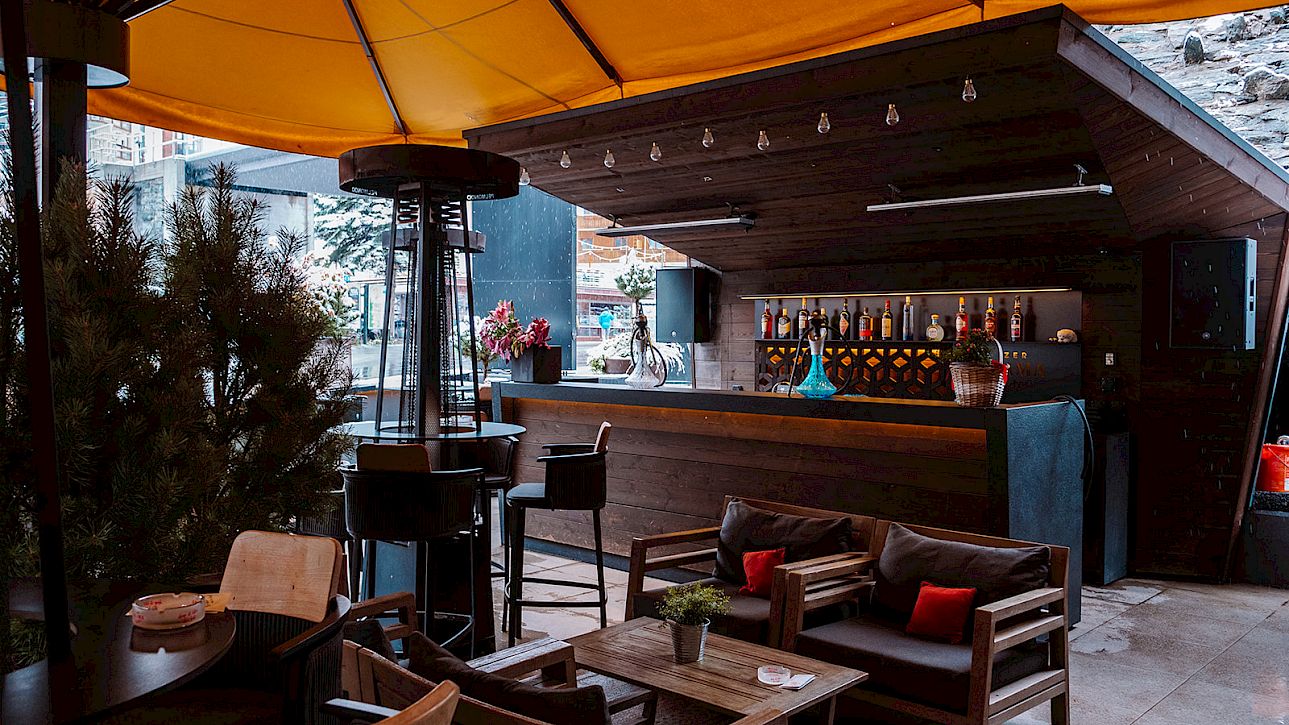 Cozy outdoor bar with yellow umbrellas, wooden furniture, and plants. Perfect for relaxed evenings.