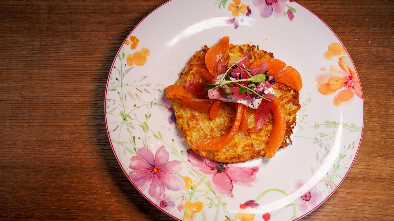 Potato pancake with salmon and herbs, served on a decorative floral plate.