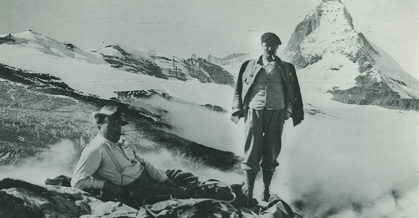 Two climbers resting with the Matterhorn in the background, surrounded by snow and clouds.