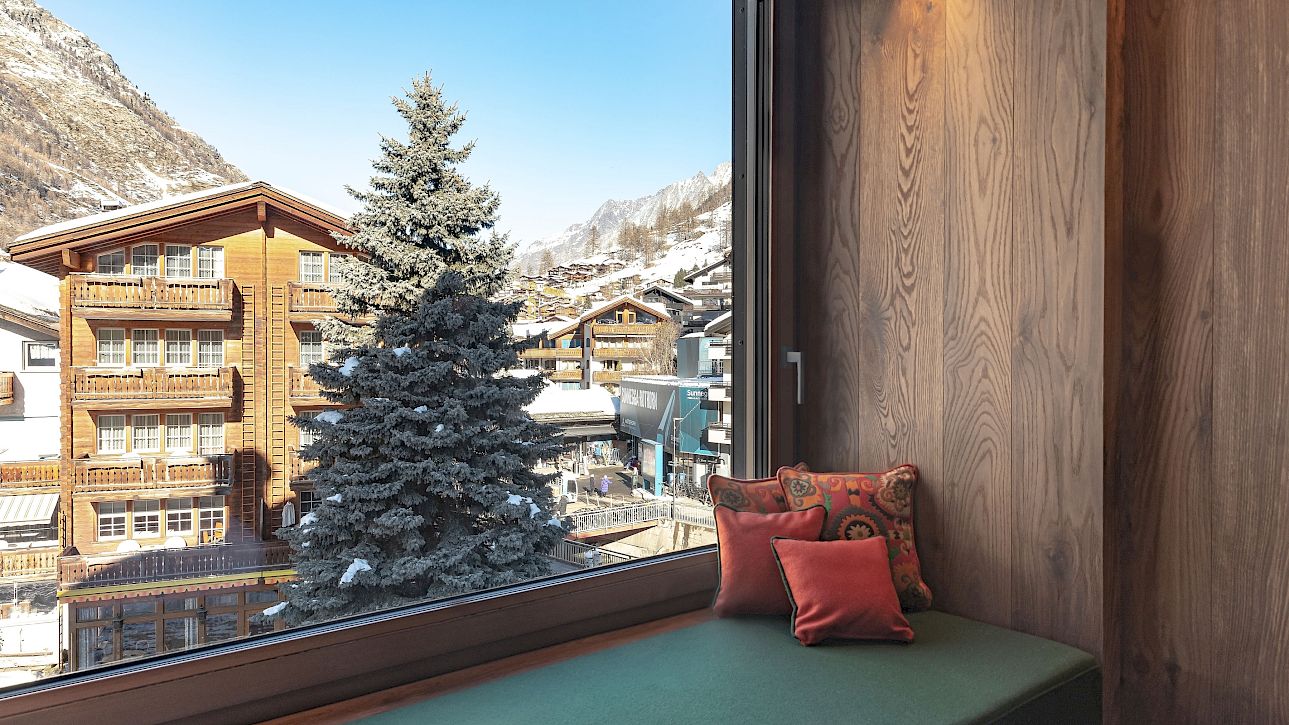 Cozy window seat with a view of snowy mountains and alpine wooden houses.