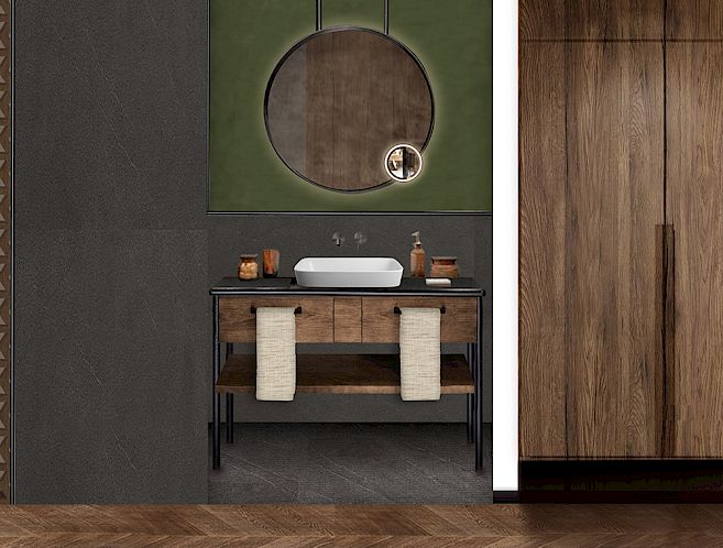 Modern bathroom with wooden furniture, round mirror, and green accent wall. Towels under the sink.