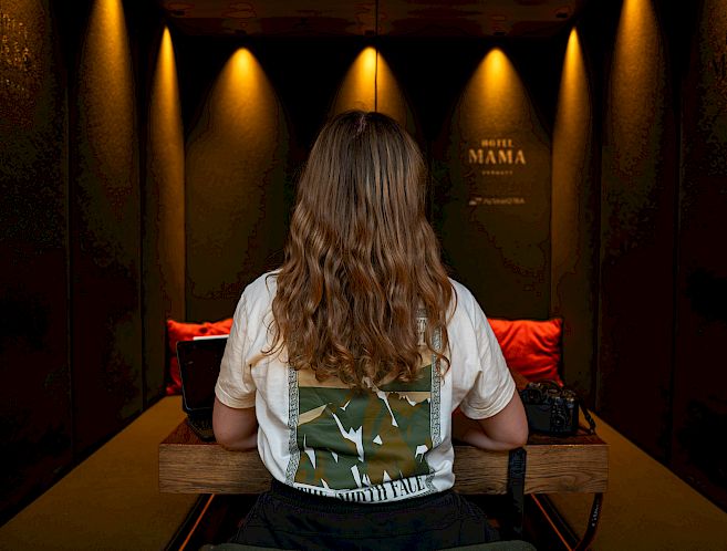 A person sits at a table in a dimly lit room, illuminated by warm lighting.