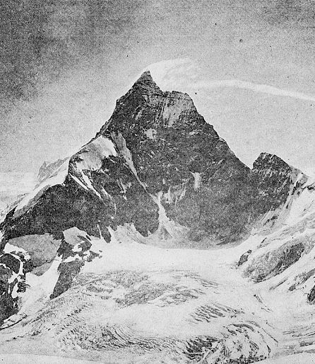 A snow-covered mountain with a prominent peak under a bright sky, surrounded by glaciers.