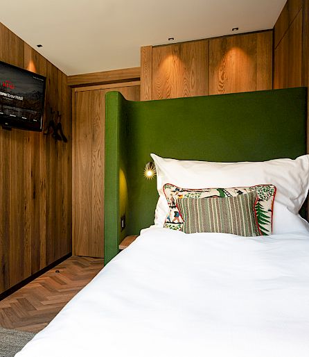 Cozy hotel room with a modern bed, wooden walls, a green headboard, and a wall-mounted TV.