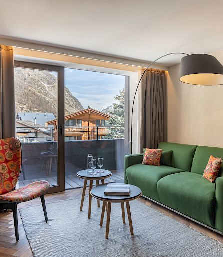 Living room with green sofa, colorful chair, coffee table, and balcony view of mountains.