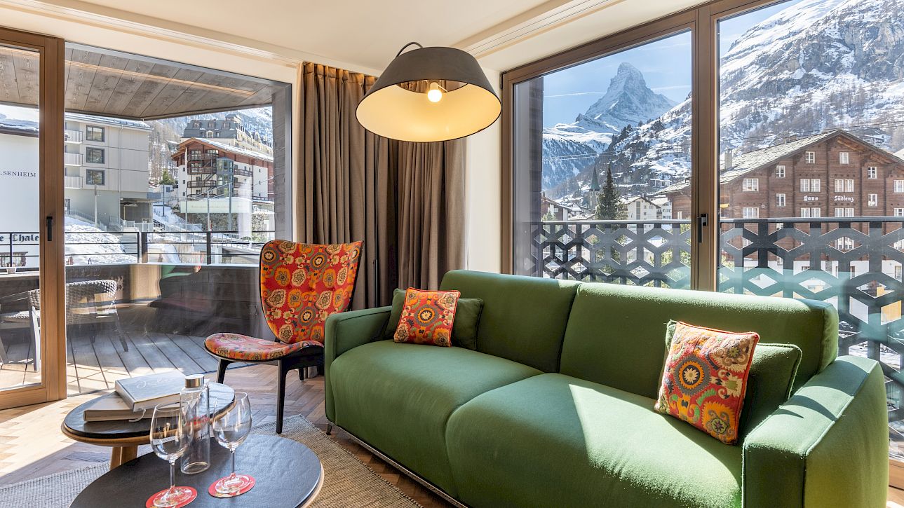 Living room with green sofa, large windows showing the Matterhorn, bright and inviting atmosphere.