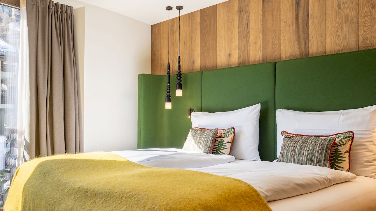 Modern hotel room with green headboard, yellow blanket, and stylish pendant lights. Bright, inviting atmosphere.