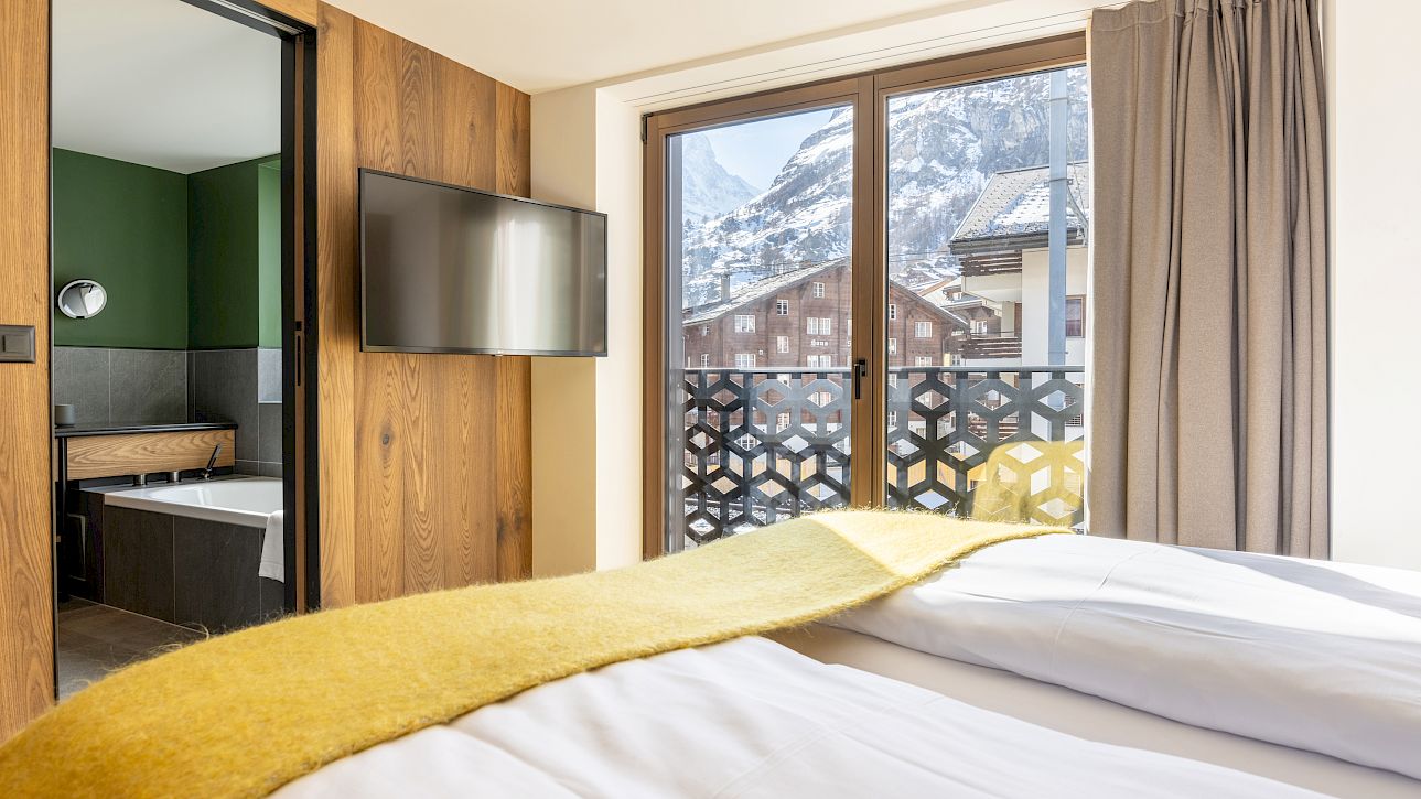 Cozy bedroom with snowy mountain view, wood walls, TV, yellow blanket, and en-suite bathroom.