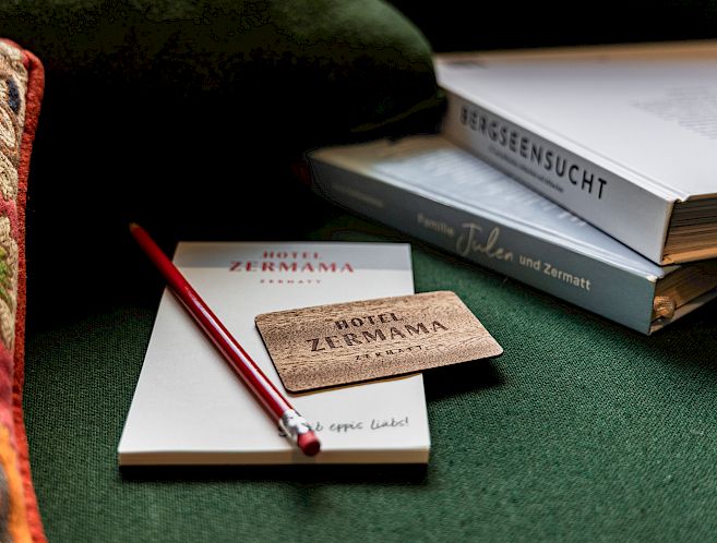 Notebook, pencil, and Hotel Zermama card on green fabric, with two books beside.