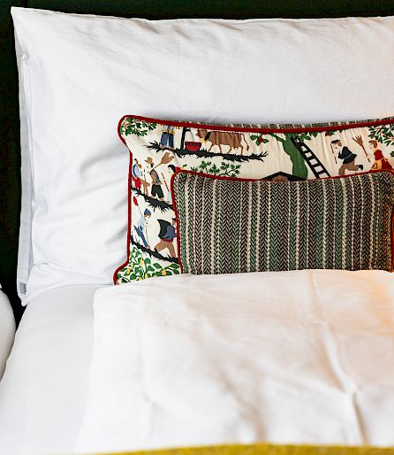 A bed with white pillows and a colorful decorative cushion in the center.