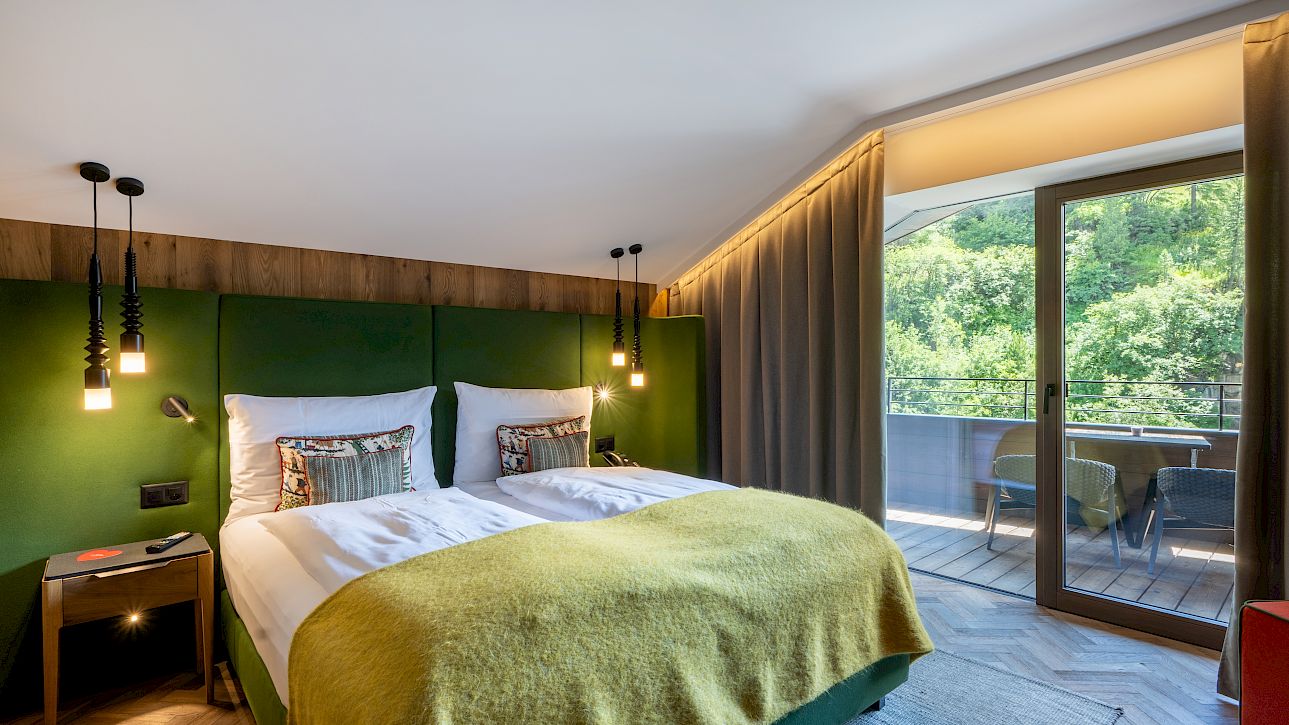 Gemütliches Hotelzimmer mit Doppelbett, modernem Dekor und Balkon mit Blick auf eine grüne Landschaft.