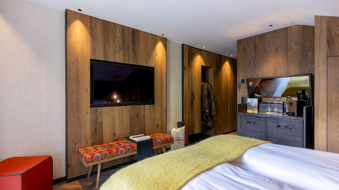Modernes Hotelzimmer mit Holzwänden, großem Flachbildfernseher, gemütlichem Bett und heller Beleuchtung.