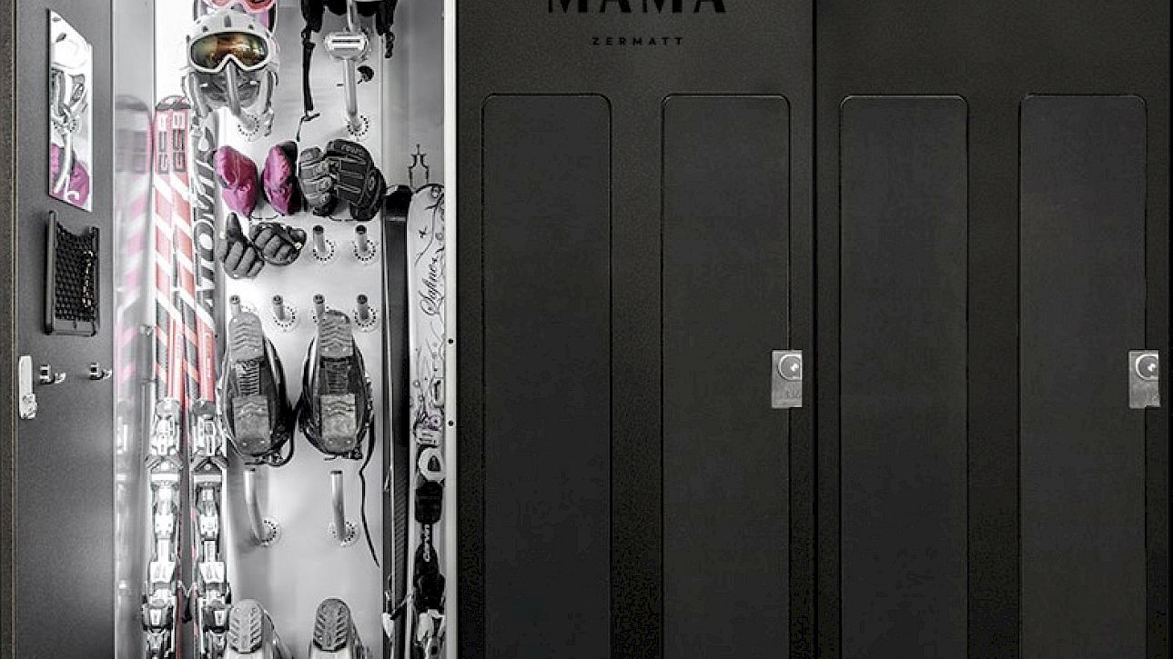 Casier ouvert dans un hôtel avec skis, bâtons et casques, à côté de casiers noirs fermés.