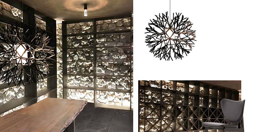 Modern room with wooden table and branch ceiling light, decorative stone wall in the background.