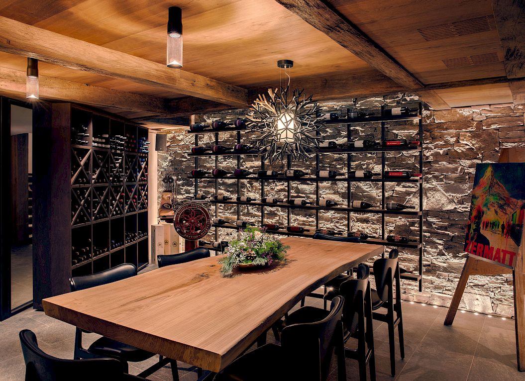 Cave à vin rustique avec table en bois, casiers à bouteilles sur mur en pierre, et éclairage élégant.