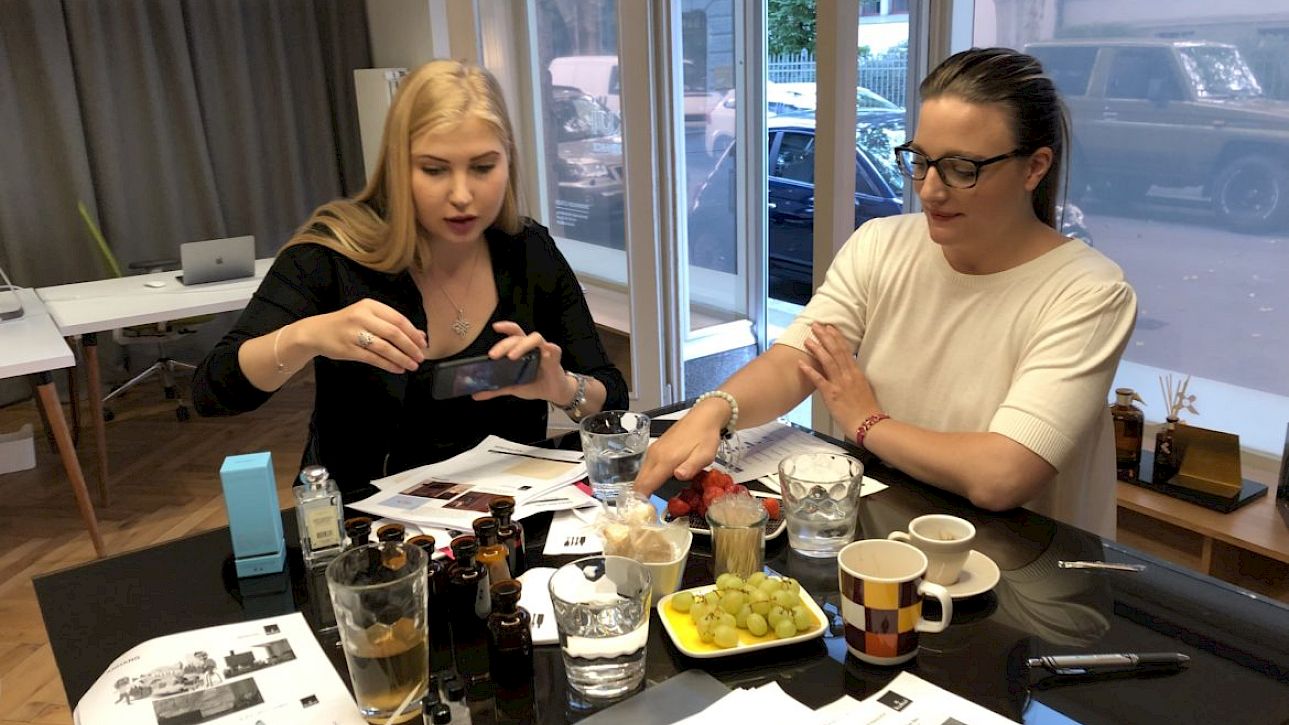 Deux femmes sont assises à une table avec des papiers et des boissons, l'une prenant une photo.
