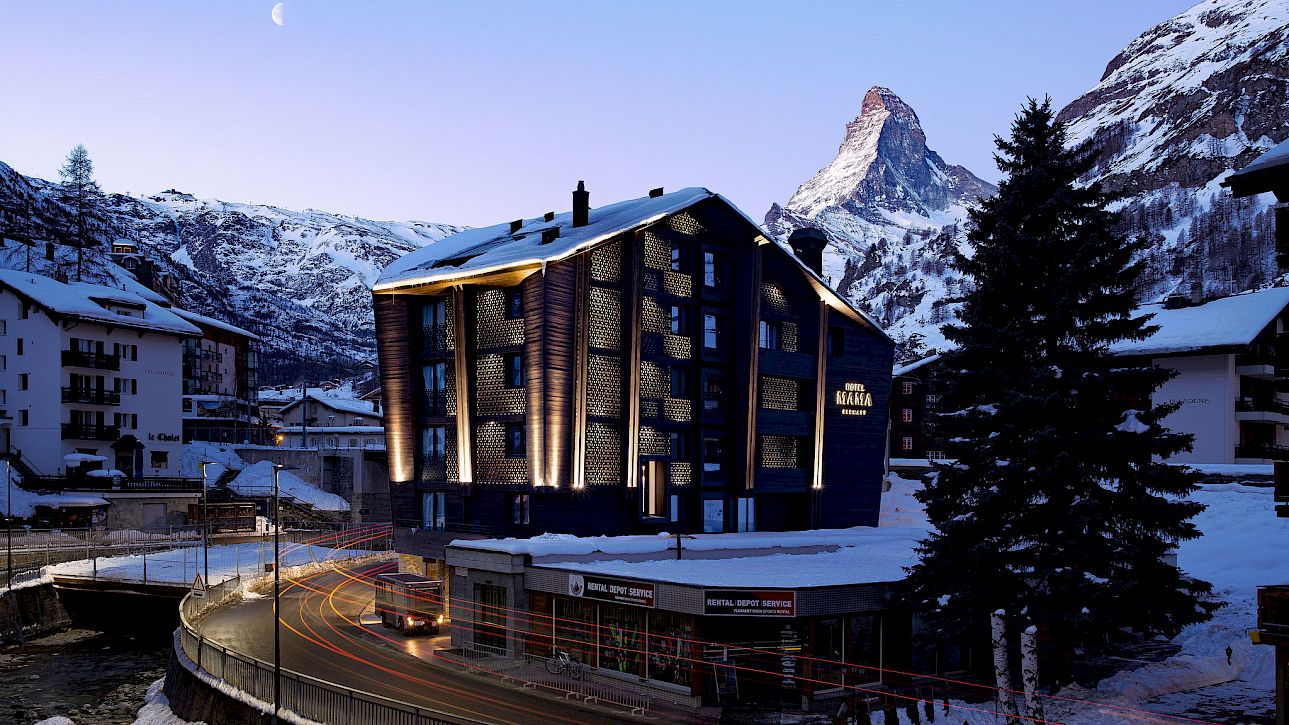 Un bâtiment moderne la nuit avec de la neige au premier plan et une montagne en arrière-plan.