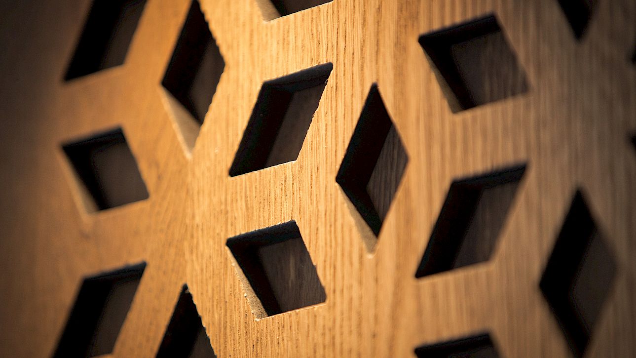 Mur en bois avec des découpes en losanges diagonaux formant un motif géométrique.