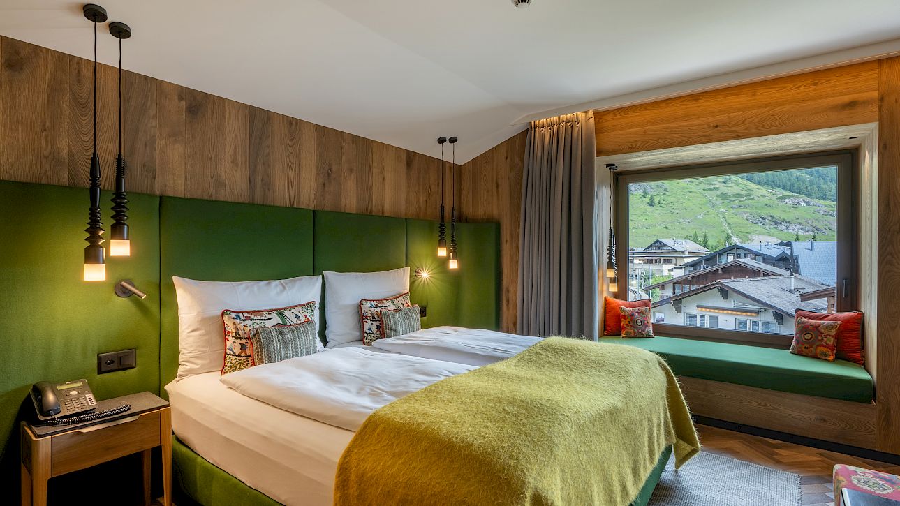 Modern hotel room with large bed, wooden decor, and a window view of the mountains.