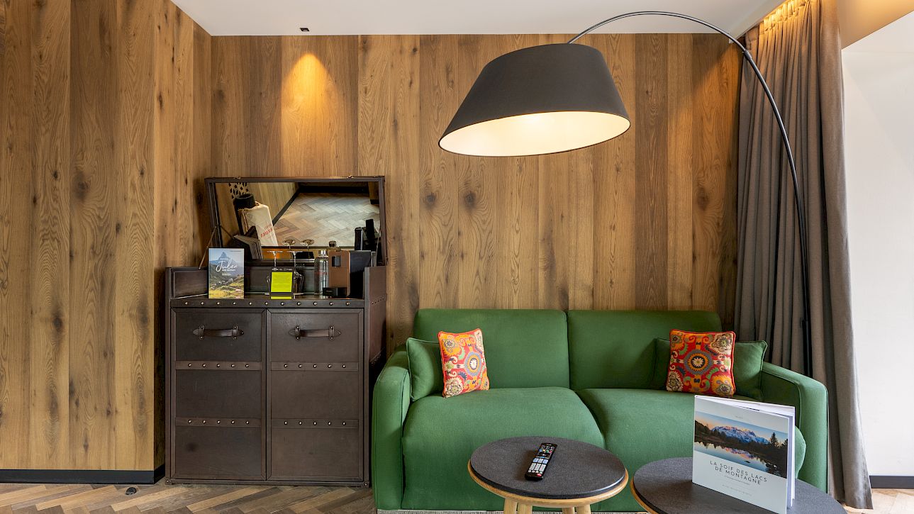 Living room with green sofa, wood wall, floor lamp, and side tables on parquet floor. Modern, cozy decor.