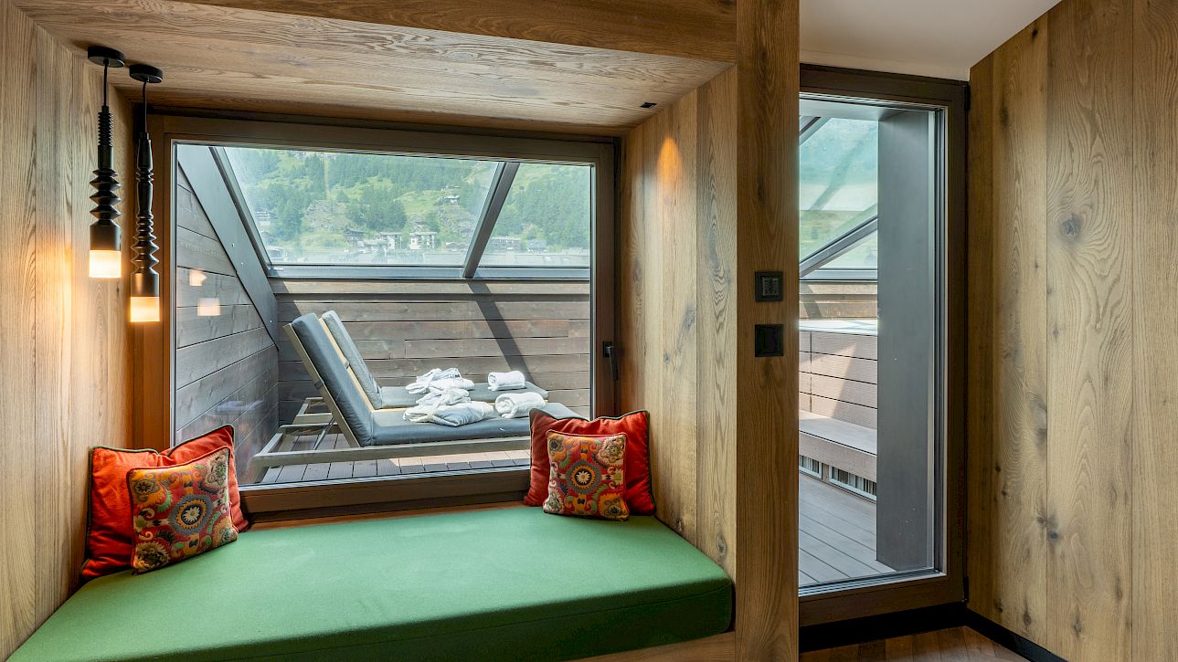 Cozy seating nook with green cushion, view of terrace and loungers through a large window.