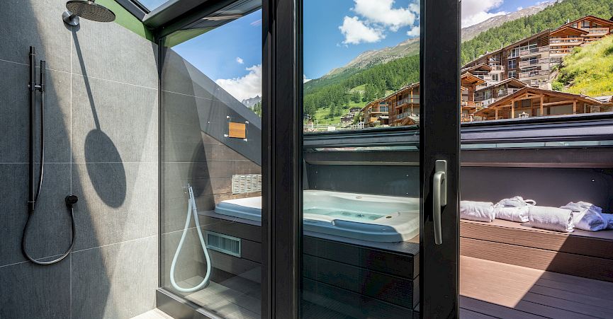 Shower with glass wall, mountain and chalet view, modern design, bright sunlight.