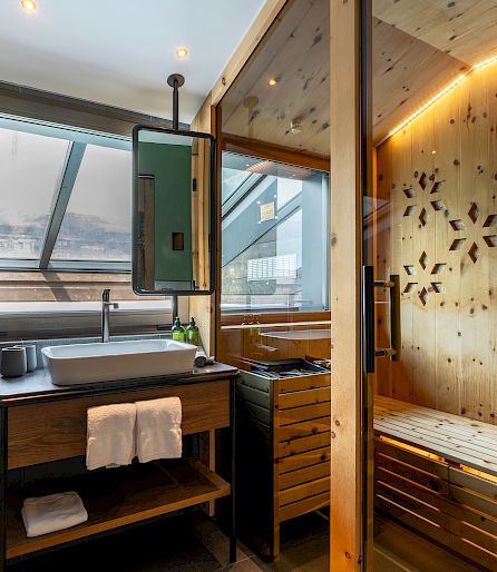 Modern bathroom with wooden sauna, sink, and towels, natural light through window.