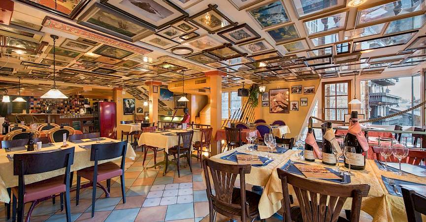 Restaurant confortable avec des tableaux au plafond, lumières chaudes, tables dressées, ambiance accueillante.