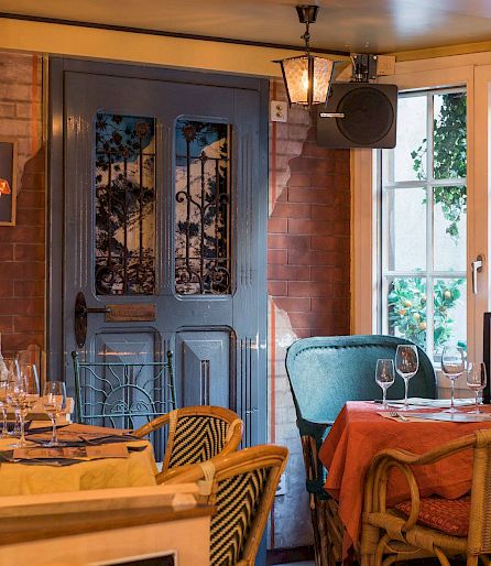 Cozy restaurant interior with set tables, wine bottles, and warm lighting.