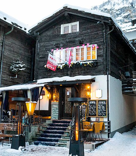 Traditional wooden house in snowy alpine scenery, with decorations and staircase; cozy winter evening.